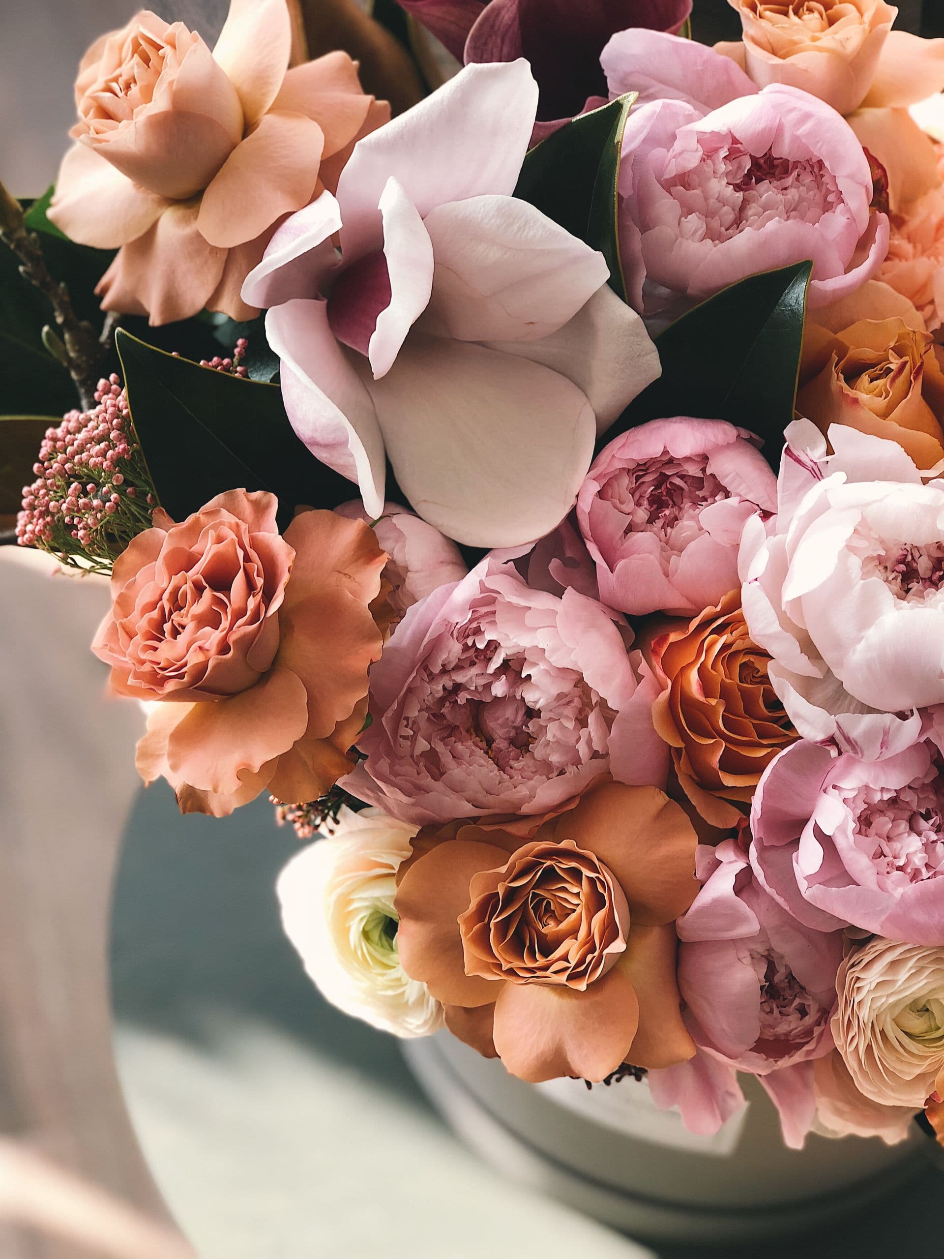 Bouquet artistique lumineux, roses et verdure dans la pénombre douce.